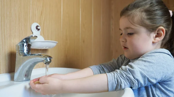 Gyönyörű lány szorgalmasan dörzsöli a kezét egy tömör szappannal a víz alatt, hogy habszivaccsal mosson kezet.. Jogdíjmentes Stock Fotók