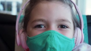 Makro, kapat. Küçük kahverengi gözlü kız kameraya bakarken yeşil maske takıyor ve pembe kulaklık takıyor. Yeni gerçeklik kavramı