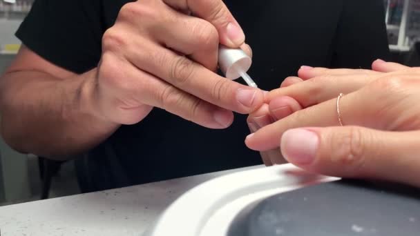 Manucure en t-shirt noir couvrant les ongles des clientes avec gomme laque incolore, les mains. Manucure professionnelle dans un salon de beauté. Hygiène et soin des mains. Concept de l'industrie beauté. Gros plan. — Video