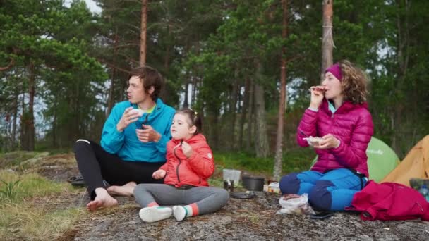 4K Tavaszi kemping családi nyaralás tó közelében fenyves erdő háttér. Két szülő és egy csinos lány együtt esznek és integetnek egy elhaladó hajónak. Családi kapcsolati tevékenység — Stock videók