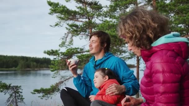 Vater inhaliert glücklich beim Frühstück im Frühlingscamp Urlaub am See, Kiefernwald Hintergrund. Zwei Eltern und eine hübsche Tochter essen Brei. Aktivität in Familienbeziehungen. — Stockvideo