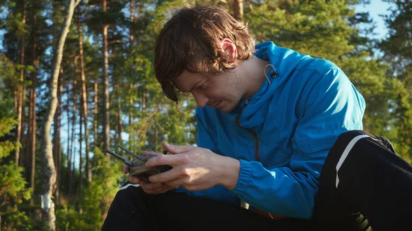 Focused young man controlling innovation aviation unmanned aircraft. Traveler using black panel of quad copter for exploring area with innovative technology taking aerial photos and videos from above