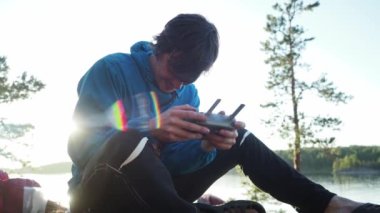 Happy smiling hiker controlles innovation aviation unmanned aircraft over sunset. Traveler uses panel of quad copter for exploring area with modern technology taking aerial photo and video from above