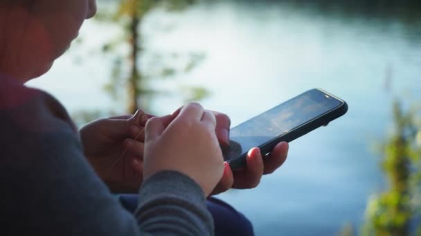 Close up. Mother using her mobile phone apps browsing chatting playing web surfing network with little daughter opposite the lake during sunset on spring camping vacation. Concept of modern technology — Stock Video