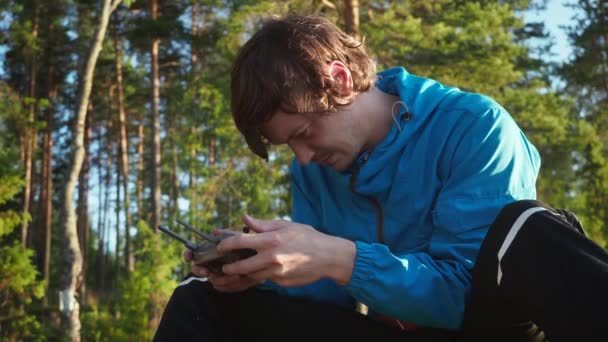 Focused young man controlling innovation aviation unmanned aircraft. Traveler using black panel of quad copter for exploring area with innovative technology taking aerial photos and videos from above — Stock Video