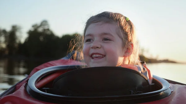 Kapatın. Sevimli kız mutlu bir şekilde gülümsüyor. Sakin bir göl kenarındaki küçük kırmızı kanoda oturuyor. Karanlık bir ormana karşı.