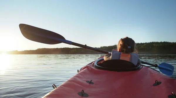 Förskola barn lära sig att segla liten röd kajak längs stor lugn sjö mot mörk skog vid ljus solnedgång på sommaren kväll — Stockfoto