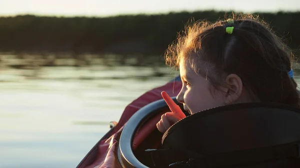 Kafkasyalı genç kız mutlu bir şey gösteriyor. Parmak kullanıyor ve kameraya gülümsüyor. Küçük kırmızı bir kanoyla sakin bir göl kenarında oturuyor.