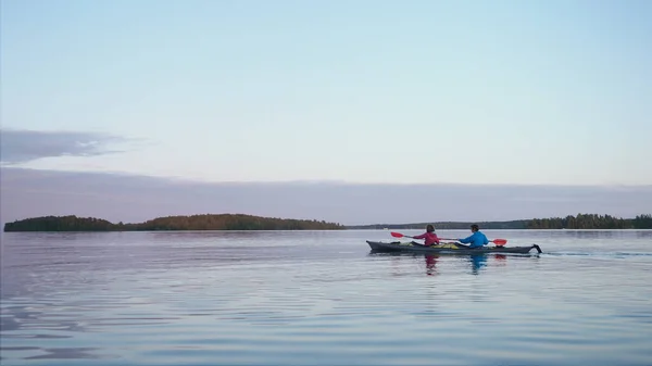 Deportes joven pareja de hombre y mujer fila pequeño amarillo plástico deportes kayak a lo largo de gran río tranquilo contra el cielo azul claro y bosque oscuro en la noche de verano —  Fotos de Stock