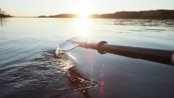 Kapky padají na vodu jezera v důsledku práce kajak veslo pádlo v modré klidné jezero při západu slunce zblízka — Stock video