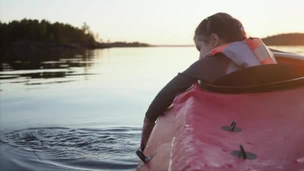 Anak kecil berusia 5 tahun bermain dengan air dan melihat tetesan air yang jatuh ke dalam air duduk di kayak merah di sepanjang danau yang tenang di hutan yang gelap — Stok Video