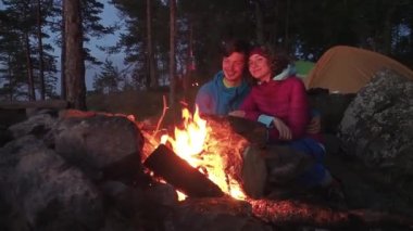 Gece geç saatlerde kamp ateşinin yanında sarılıp gülümseyen mutlu bir çift genç adam ve kadın. Tatilde aile hayatı kavramı. Yavaş çekim