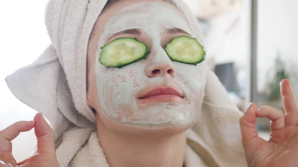 Young pretty woman with cosmetic carbo detox clay light green mask put slices of cucumber, covering eyes and relaxing. Girl takes care of oily skin complexion. Beauty treatment. Skincare — Stock Photo, Image
