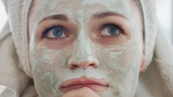Kapatın. Güzel bir kadın aynanın önünde yüzünde kozmetik detoks kil açık yeşil maske bekliyor. Yağlı cilt cildiyle ilgilenen bir kız. Güzellik tedavisi. Cilt bakımı