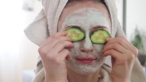 Mujer bonita joven con máscara de desintoxicación de carbohidratos cosméticos de color verde claro máscara poner rebanadas de pepino, cubriendo los ojos y relajante. Chica se encarga de la tez de la piel grasa. Tratamiento de belleza. Cáscara — Vídeo de stock