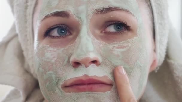 Közelről. Gyönyörű női várakozási idő kozmetikai szénhidrát méregtelenítő agyag világos zöld maszk az arcán előtt egy tükör. A lány, aki az olajos bőrt ápolja. Szépségápolás. Bőrápolás — Stock videók