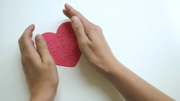 Kadınların üst görüntüsü. İki el de dikkatli sarılma. Kırmızı kalp şeklinde yapboz.