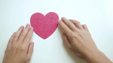 Kadınların ellerine yukarıdan bakıldığında kırmızı kalp şeklinde yapboz beyaz masa arkasındaki kağıt bloklarından alınır.