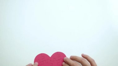 Kadınların ellerinin üst görüntüsü, kağıt bloklarından beyaz masa arka planına kadar kırmızı kalp şeklinde yapboz şeklindedir.