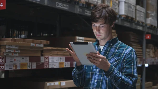 Kapatın. Geniş bir depoda, yüksek raflarda duran karton paketlerde tabletleri kontrol eden genç esmer adam.