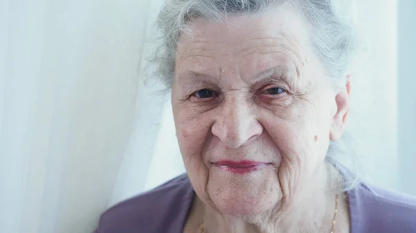 Kahverengi gözlü, büyük kırışıklıkları olan yaşlı beyaz saçlı büyükanne yüzünü kapat. Uzun ve sağlıklı yaşam süresince doğal güzellik. Muhteşem son sınıf öğrencisi ve çekici bir kadın.