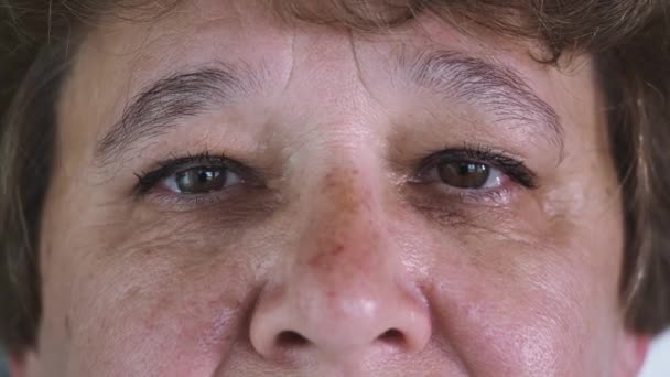 Primer plano de 50 años cara femenina con hermosos ojos marrones, grandes arrugas en la cara de las mujeres de edad. Belleza natural con pecas. Mujer hermosa con pestañas largas y aspecto atractivo — Vídeos de Stock