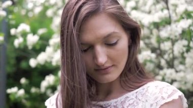 Bahçede çiçek açan elma ağacının yanında duran güzel beyaz elbiseli, uzun, kahverengi tavşanlı kızın yakın plan portresi. İlkbaharda çiçekli bahçede çekici bir genç kız.