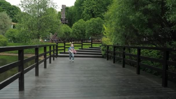 7月4日に独立を祝う、アメリカの休暇中に遊園地で実行されているポニーテール、愚かな角と面白いクローク国の色を持つ幸せな笑顔愛国的な女の子 — ストック動画