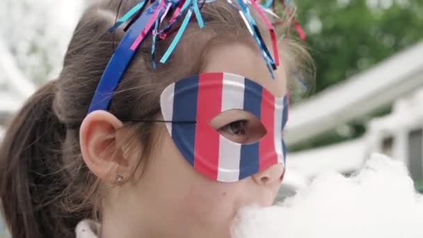 Szczęśliwy biały dziewczynka w USA symbol karnawał zabawna maska i głupie rogi zjada waty cukrowej, uśmiechy korzystających 4 lipca uroczystości na zewnątrz w parku rozrywki, Ferris koło tła — Wideo stockowe
