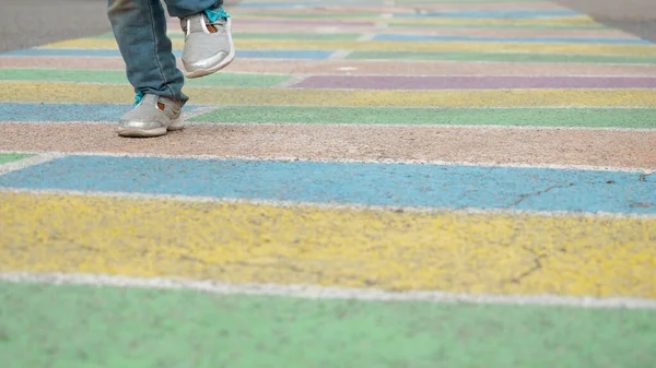 Copy spase. Little fun girl jumping active on colorful long hopscotch game painted on asphalt, playing classics without numbers in squares outdoors dreaming of happiness. Childhood kid dream concept