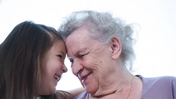 Anaokulunda gülümseyen tatlı küçük kız olgun büyükanne dadının alınlarının birbirine dokunmasına bakıyor. İki kuşak büyükbaba ve torun aile içinde keyif, saygı ve sıcak akrabalık sahibi. Kapat.