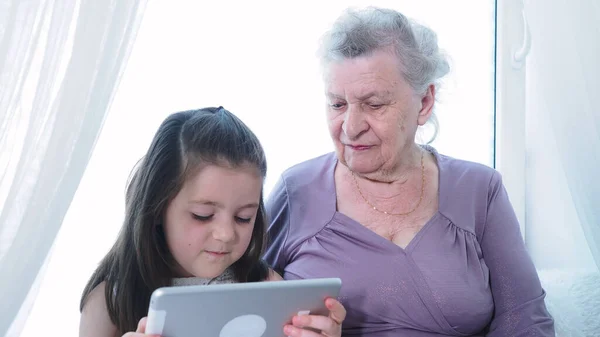 Kapatın. Küçük tatlı bir anaokulu kızı yaşlı büyük anne dadıya dijital tablet kullanmayı öğretiyor. İki kuşak aile büyükbabası ve torunu yeni teknolojiler keşfediyor. Evde ped cihazı teknolojisi.