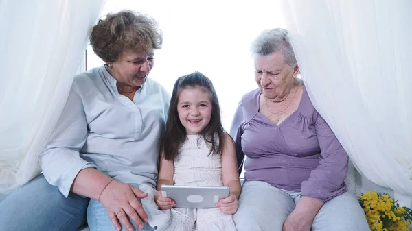 Happy cute preschool girl with digital tablet around her family old great-grandmother and grandma nanny. Three generation female family enjoy, respect and warm relation at home, white background