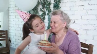 Mutlu gülümseyen küçük tatlı kız 85. yaş gününde büyük annesine sarılıyor ve onu öpüyor. Yaşlı kadın elinde sönmüş mumla pasta tutuyor. Tadını çıkar, saygı duy ve sıcak ilişki kur. Kutlama konsepti