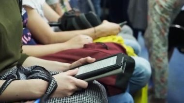 Kadın metro istasyonunda diğer insanların arka planlarında e-kitap okuyor..