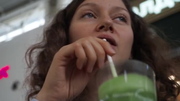 Attractive woman drinking green smoothie in a mall restaurant. Close up — Stock Video