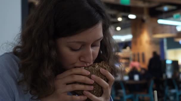 Belle femme affamée mangeant un sandwich dans un restaurant de centre commercial. Gros plan — Video