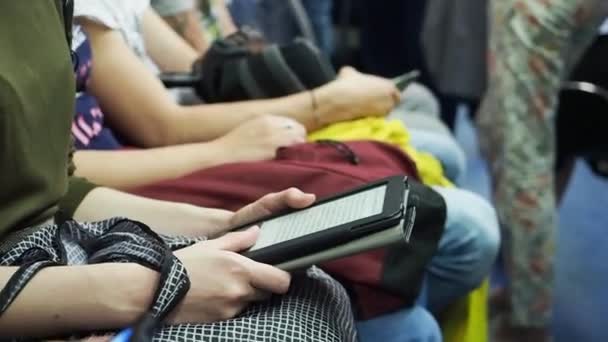 Woman reads e-book in subway train at metro on the backgrounds of other people. — Stock Video