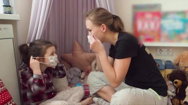 Anne kızının tıbbi maske takmasına yardım ediyor. Ev karantinası.