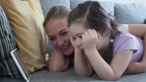 Ευτυχισμένη οικογένεια μητέρα και μικρή κόρη βλέποντας κινούμενα σχέδια χρησιμοποιώντας ψηφιακή ταμπλέτα και γελώντας στον καναπέ στο σπίτι κατά τη διάρκεια της κοινωνικής αποστασιοποίησης και της αυτο-απομόνωσης σε καραντίνα για Coronavirus — Αρχείο Βίντεο