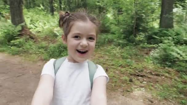 Felice, eccitata ridendo piccola ragazza fa selfie video alla fotocamera dello smartphone e gira durante la passeggiata nel parco estivo. Infanzia felice, inseguire i sogni, stile di vita avventura. Punto di vista colpo da vicino — Video Stock