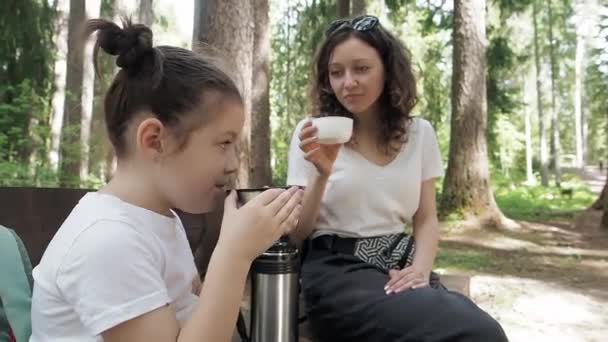 Voyageur mère et fille buvant du thé chaud dans une tasse thermos pendant la randonnée estivale en forêt. Bonne famille profiter d'une boisson chaude dans une tasse de thermos. Rafraîchissements et moments de détente pendant le voyage de vacances — Video