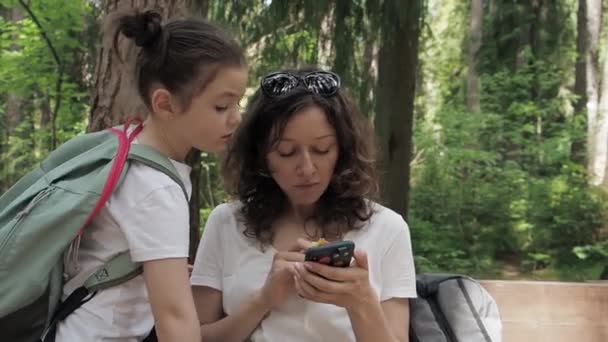 หญิงและลูกสาวนักท่องเที่ยวที่หายไปพร้อมกระเป๋าเป้นั่งมองหาทิศทางตรวจสอบเส้นทางบนโทรศัพท์มือถือโดยใช้ GPS ในป่า สัมผัสหน้าจอแบบใกล้ชิด — วีดีโอสต็อก