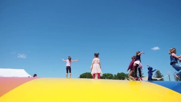 Los niños felices se divierten saltando juguetonamente en el parque de atracciones amarillo del trampolín durante el fondo azul del cielo del verano. Hermoso concepto de infancia — Vídeo de stock