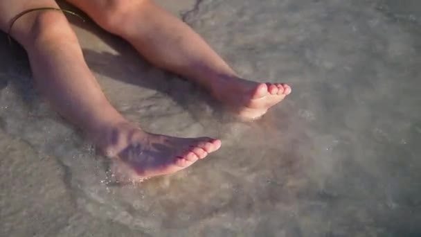 Вид сверху. Дети Ноги на берегу морского песка брызгают водой волной над загорелыми женскими ногами на пляже. Мбаппе в отпуске или в путешествии в солнечный день летом. Медленное движение — стоковое видео