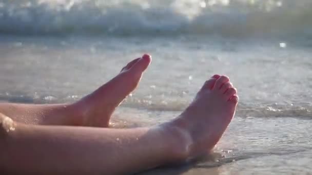 Girls Piernas en la playa de arena marina salpicando olas de agua sobre los pies femeninos bronceados en la playa. Concepto de vacaciones o viajar en un día soleado en verano. Movimiento lento — Vídeo de stock