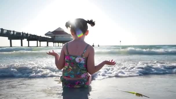 Девушка, сидящая на берегу песчаного пляжа, брызгает волной на загорелые ноги. Мбаппе в отпуске или в путешествии в солнечный день летом. Медленное движение — стоковое видео