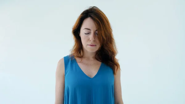 Stüdyodaki beyaz duvarın arkasında tek başına duran mavi gözlü, sevimli kızıl saçlı genç kızın portresi. Güzellik konsepti