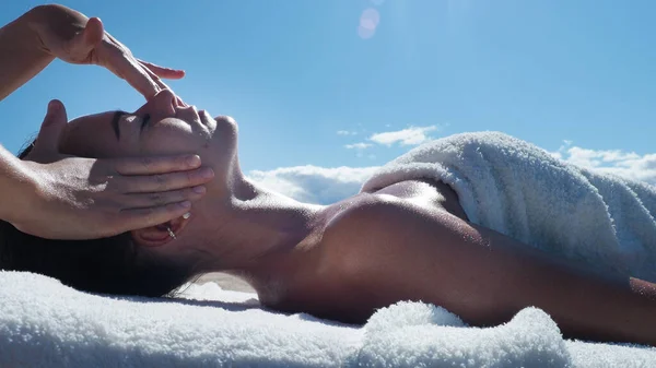 Kapatın. Yazın kumsalda esmer kıza yüz masajı yapan masaj terapisti. Stresten rahatlama, baş ağrısı, sağlık spa, yaşam tarzı ve vücut bakımı, rehabilitasyon konsepti