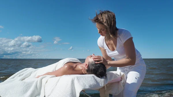 Yaz tatilinde kumsaldaki esmer kıza yüz masajı yapan kadın masaj terapisti. Stresten rahatlama, baş ağrısı, sağlık spa, yaşam tarzı ve vücut bakımı, rehabilitasyon konsepti